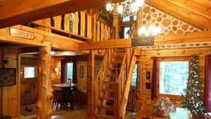 L’intérieur d’un chalet rustique, avec des murs en bois, un coin repas, un escalier et un sapin de Noël.
