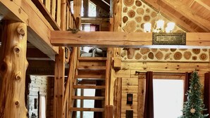 L’intérieur d’un chalet en bois, avec un escalier, un petit coin cuisine et un sapin de Noël.