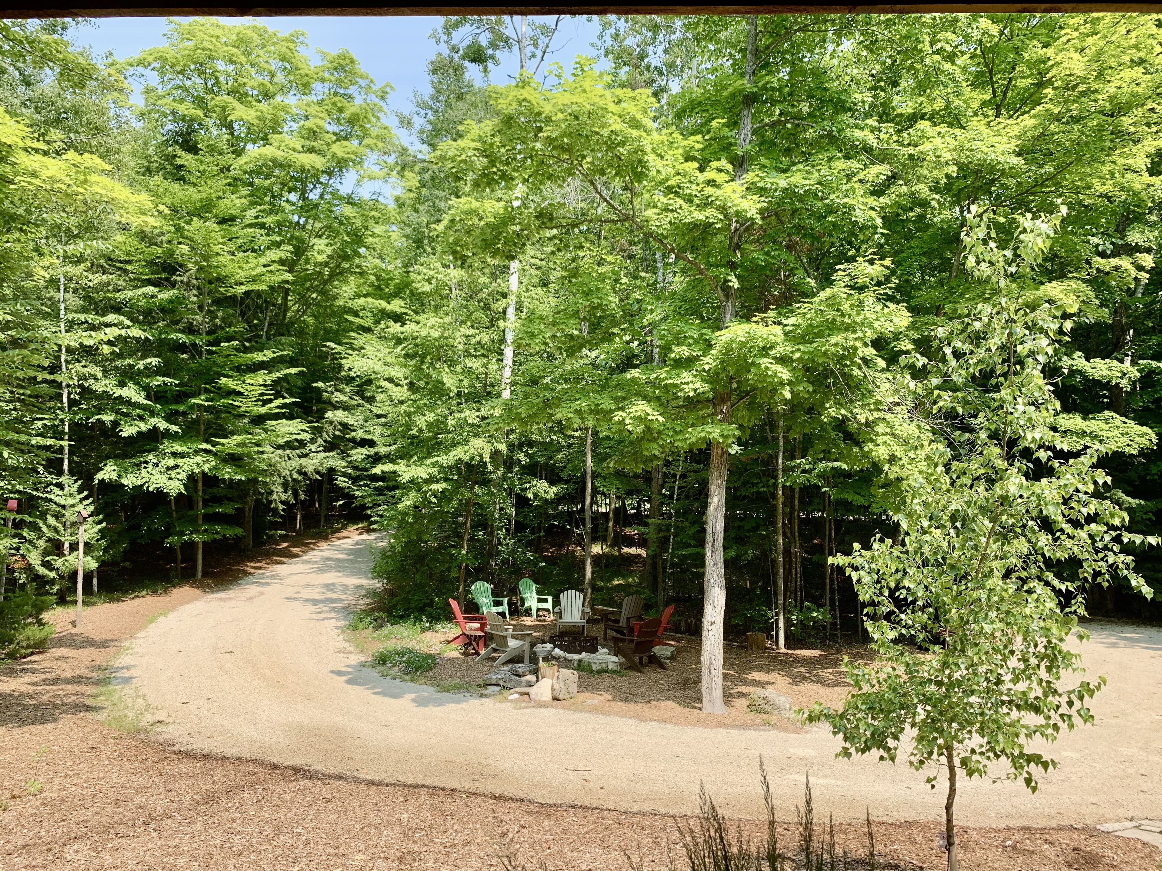 Un camping con un sendero de grava que lleva a una mesa de picnic rodeada de sillas Adirondack.