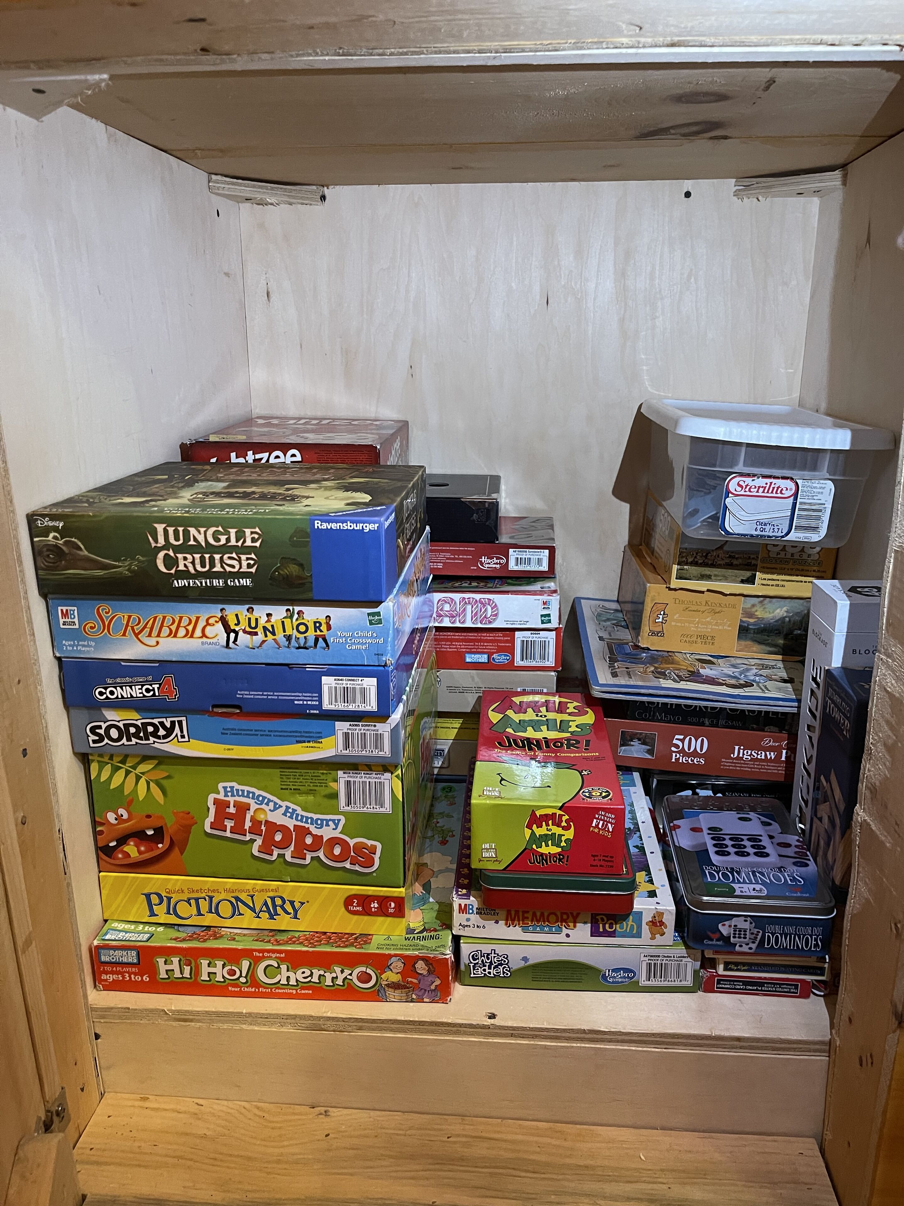 A storage area with various board games and a container of Sterilite.