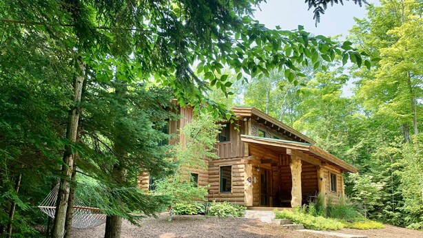 Une cabane en rondins dotée d’un porche, entourée d’une forêt dense.