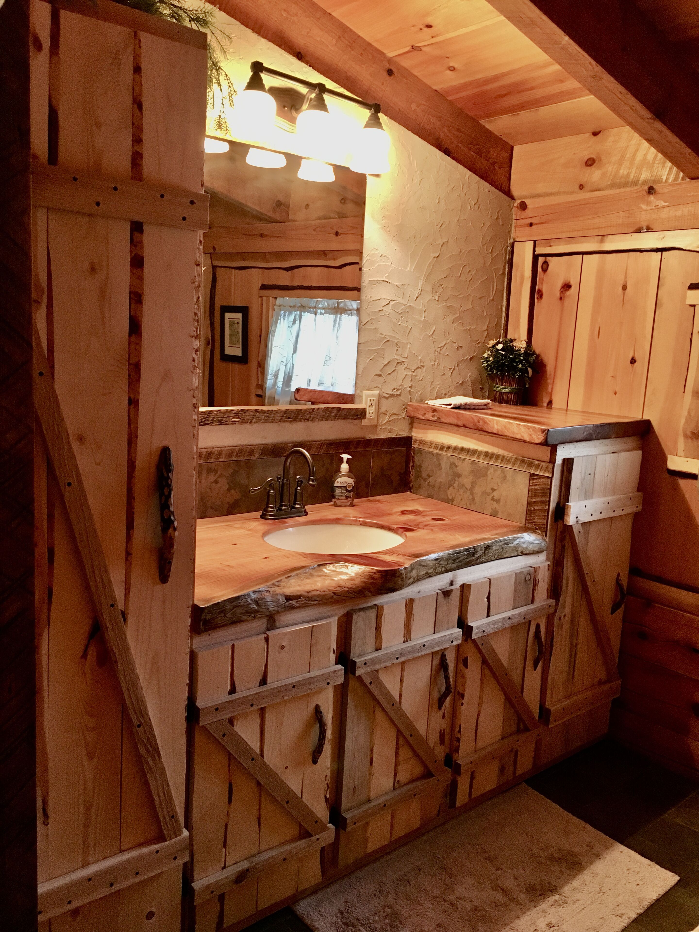 A rustic wooden bathroom with a large sink, wooden cabinets, and a mirror above the sink.