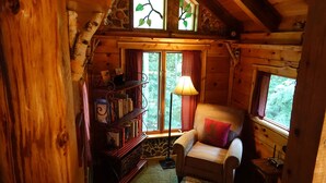 L’intérieur d’un chalet chaleureux, avec une bibliothèque en bois, un fauteuil confortable et une lampe.