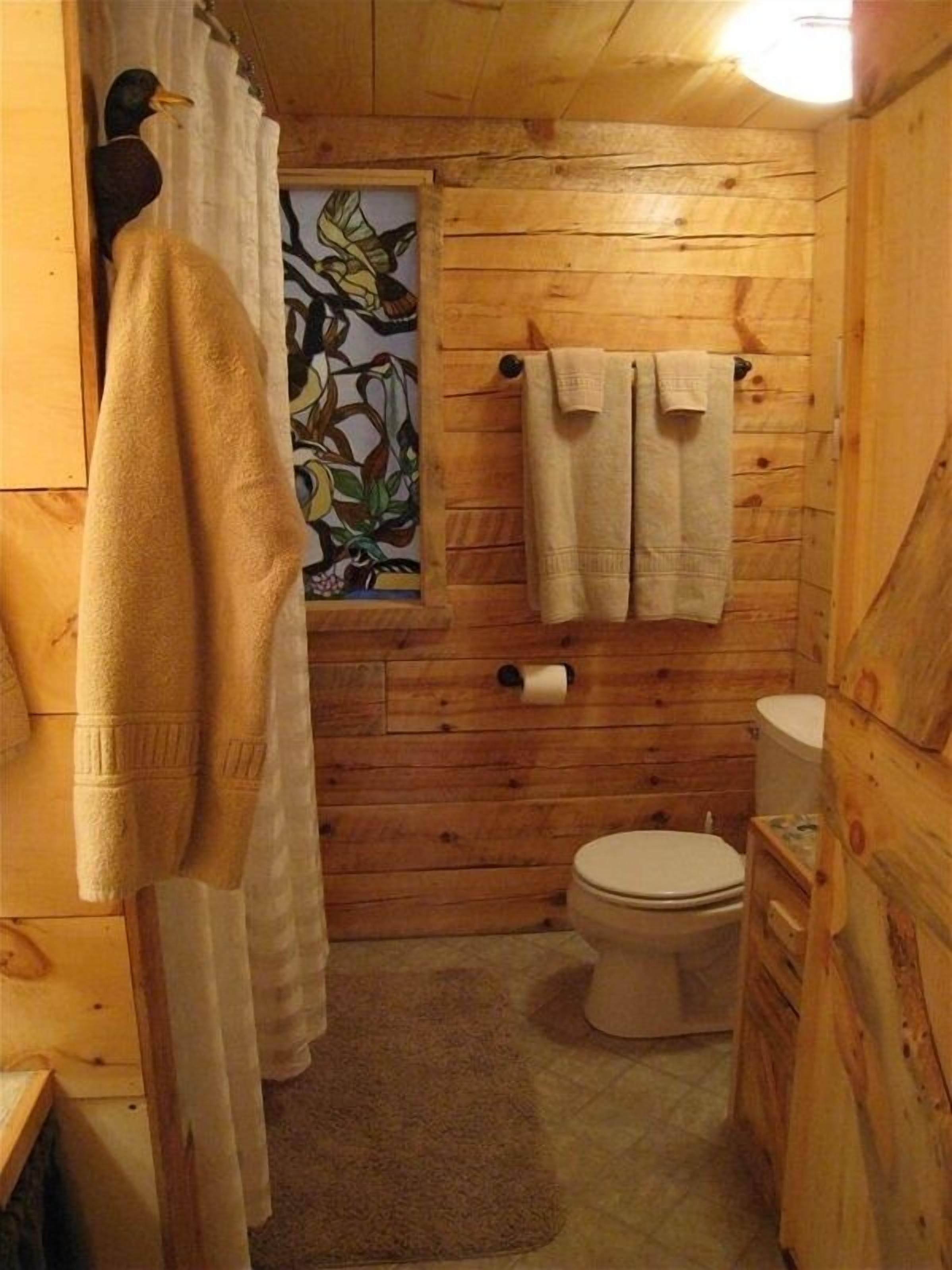 A wooden cabin bathroom with a toilet, a towel rack, and a shower curtain.