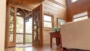 Ein Holzinterieur mit einer Schiebetür, die auf einen Balkon führt, einem Holztisch mit einer Pflanze und einem Bett mit weißer Bettdecke.