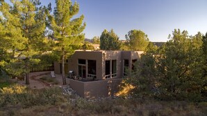 Une maison moderne, de plain-pied, dotée de grandes fenêtres et entourée d’un paysage naturel, avec des arbres et un ciel dégagé.