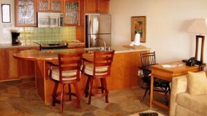 A kitchen with a central island, wooden chairs, a refrigerator, and a microwave. - Quite Simply THE BEST Kona Reef Oceanfront. (Kailua Kona)