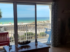 Een balkon met uitzicht op het strand, een tafel met een schaal fruit, en een rode stoel.