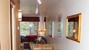 A cozy interior with a wooden dining table, chairs, and a bench. There are ceiling lights and a window with a view of trees.