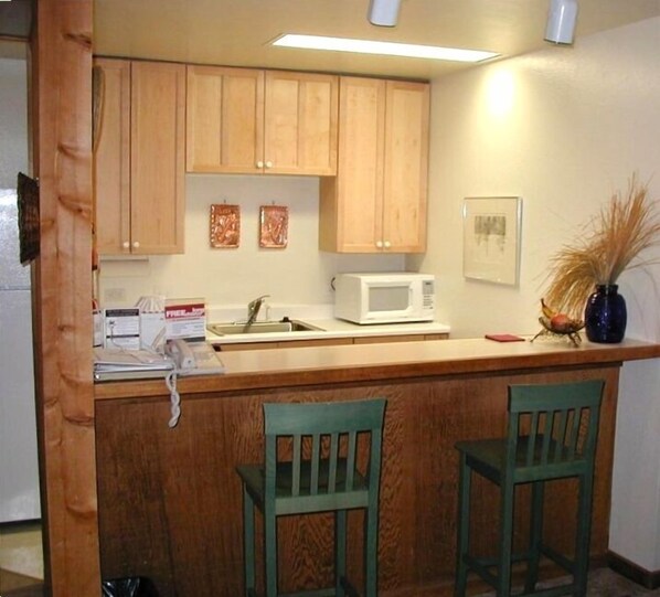 A kitchen with wooden cabinets, a microwave, and two green chairs.