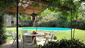 Un patio techado con mesa y sillas, un farol colgante y una piscina al fondo.