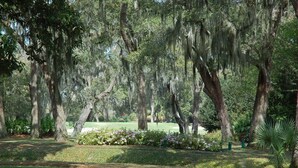 Un parque con árboles maduros, un césped bien cuidado y un campo de golf al fondo.
