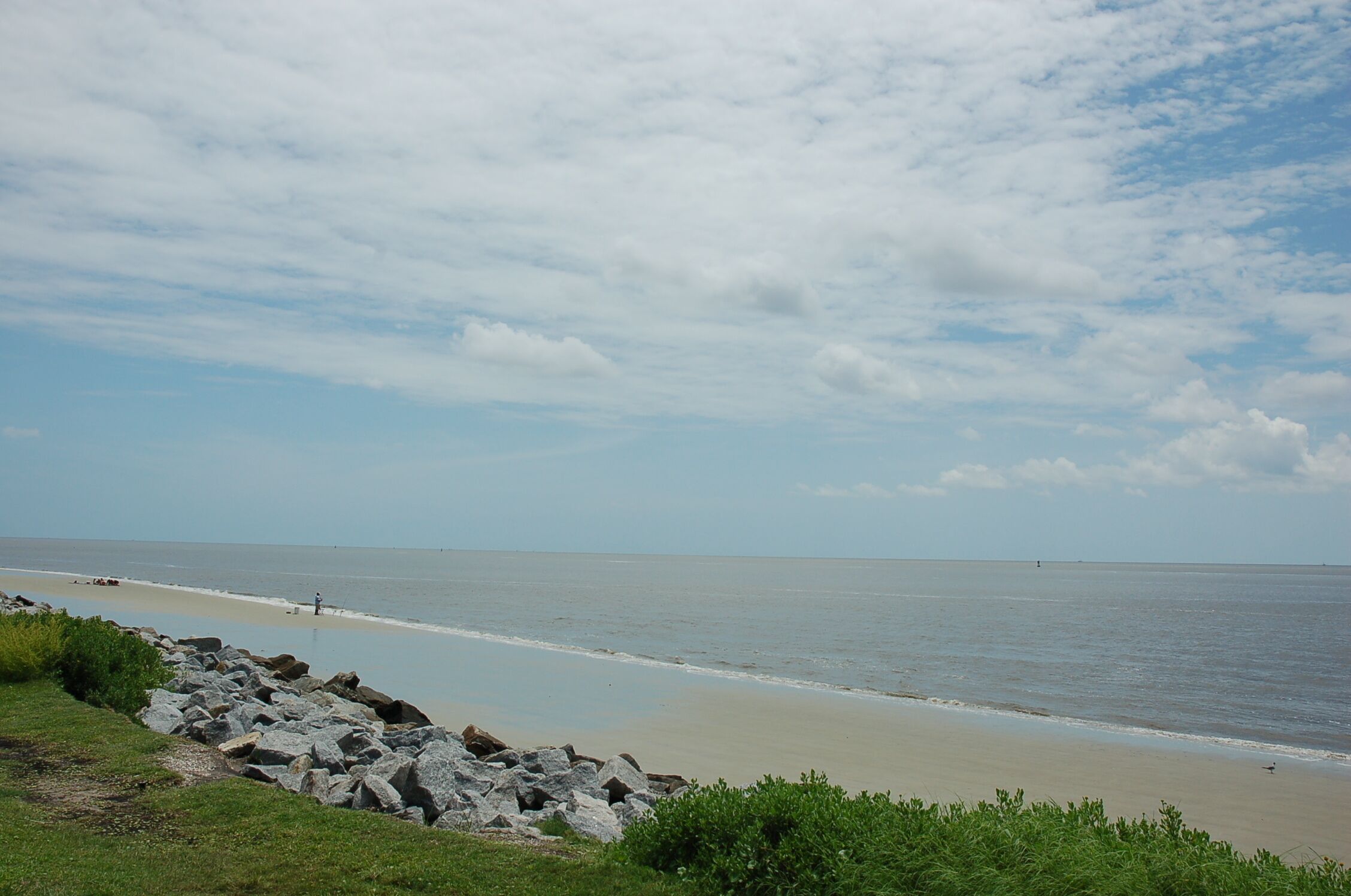 Een strand met een rotsachtige kustlijn, een heldere lucht en rustig water.