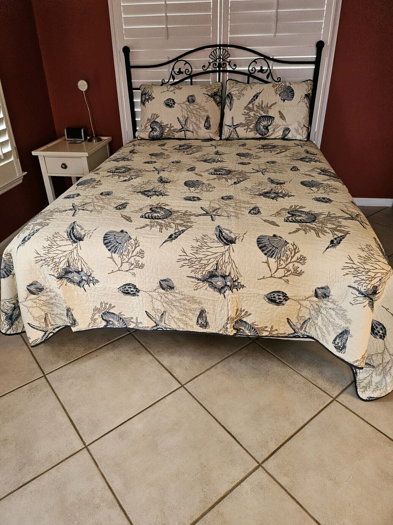 A bed with a patterned bedspread, a metal headboard, and a bedside table with a lamp.