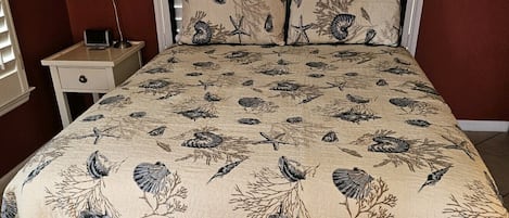 A bed with a patterned bedspread, a metal headboard, and a bedside table with a lamp.