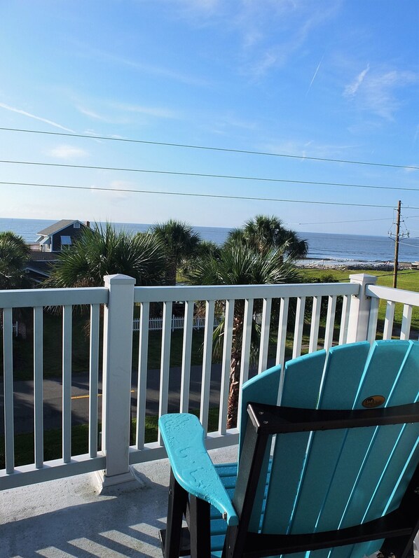 A balcony with a view of the ocean, a white railing, and a blue chair.