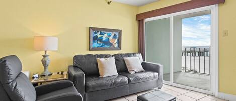 A living room with a sofa, armchair, and ottoman, a lamp, and a painting on the wall.