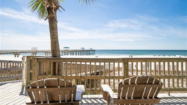 A wooden deck with two chairs and a table, overlooking a beach with a pier in the distance. - Million Dollar View from Your Balcony! (Orange Beach)