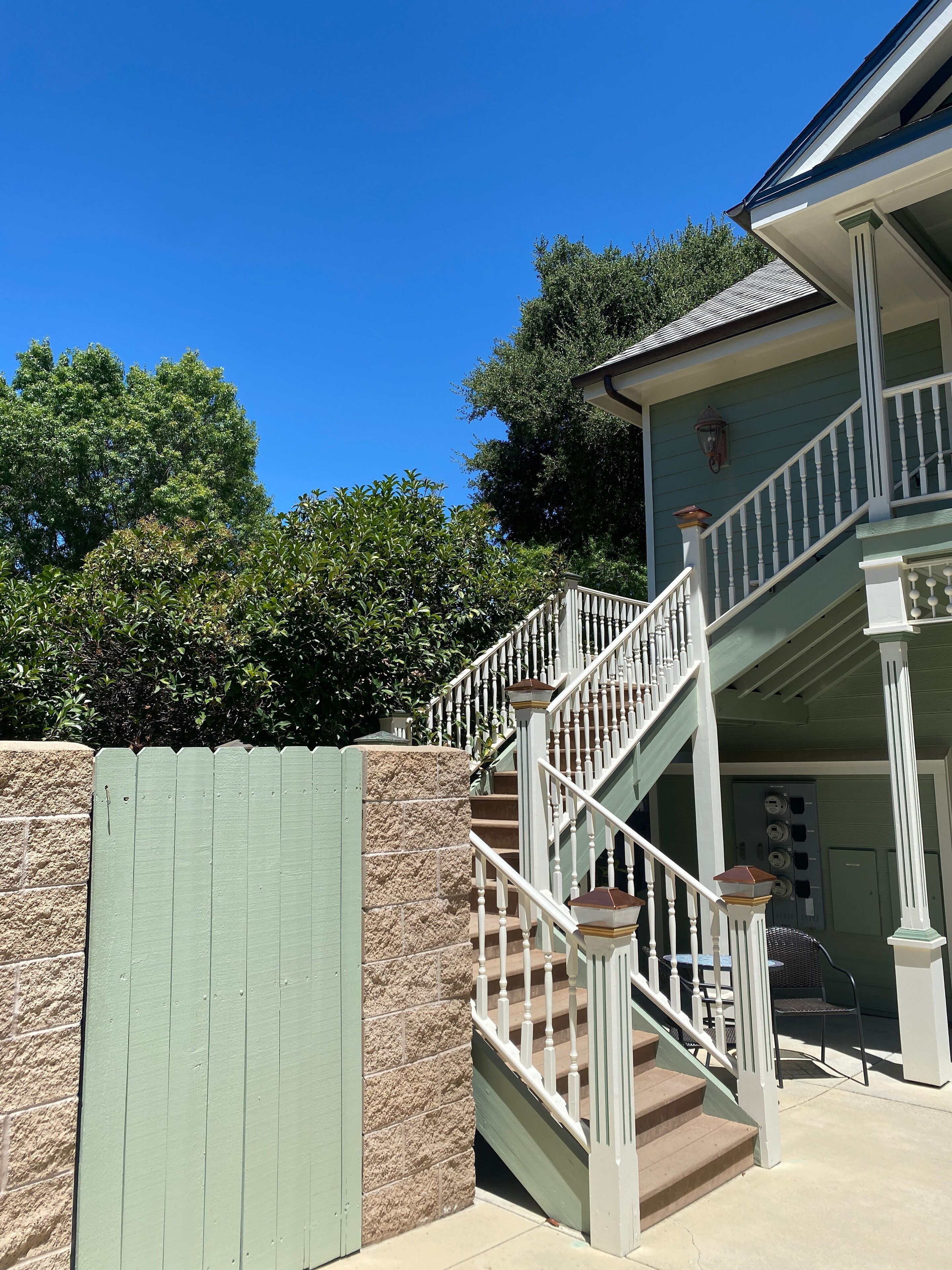 A two-story house with a staircase, a stone wall, and a green fence.