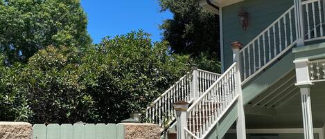 A two-story house with a staircase, a stone wall, and a green fence.