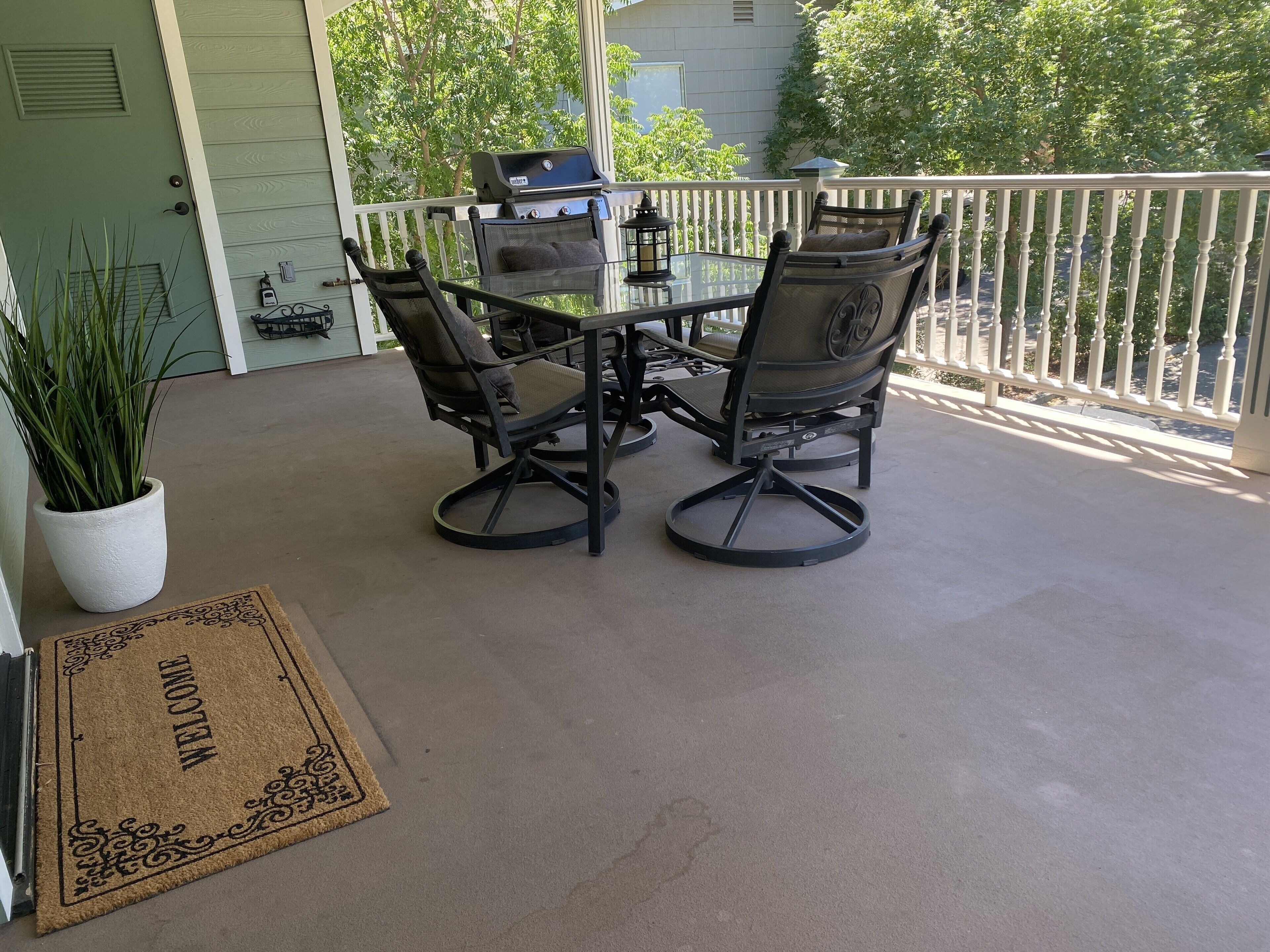 A patio with a table and chairs, a grill, and a potted plant.