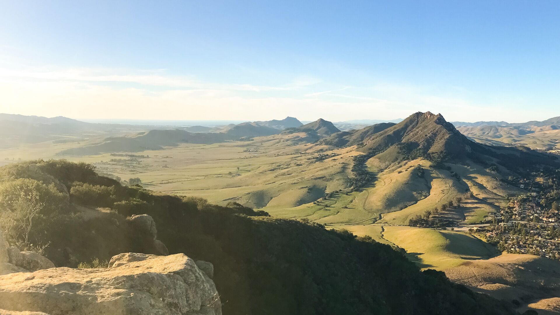 A mountainous landscape with a prominent peak, a valley with scattered buildings, and a clear sky.