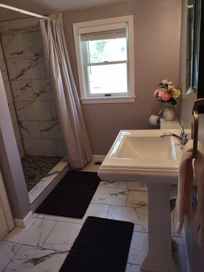 Une salle de bain avec une douche, un lavabo, une fenêtre et un vase de fleurs.