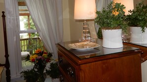 Une commode en bois surmontée d’une vitre, un vase blanc rempli de fleurs et une plante en pot.