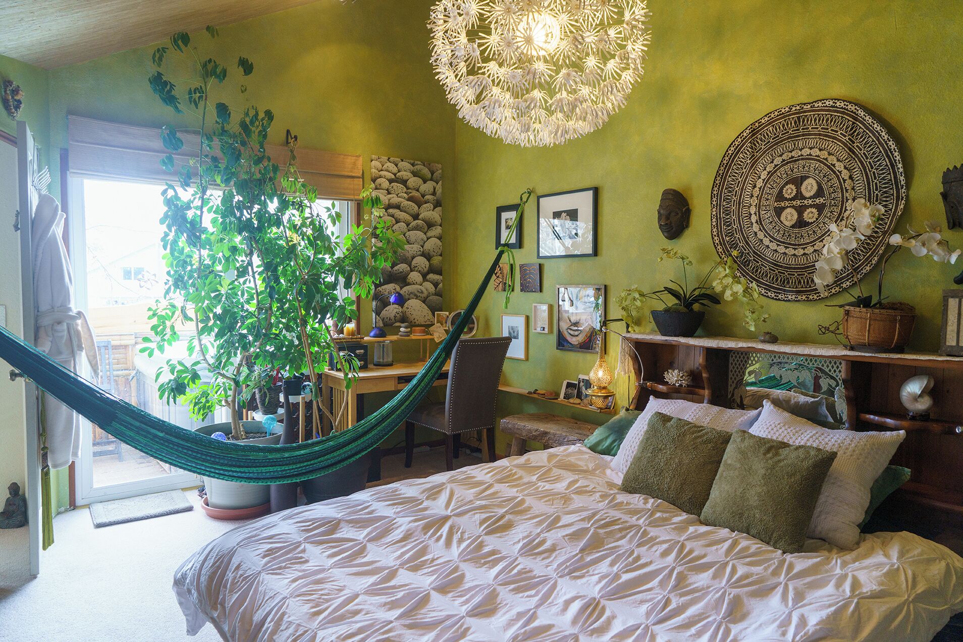 A bedroom with a bed, a hammock, a desk, and various decorative items.