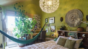 Een slaapkamer met een bed, een hangmat, een bureau en diverse decoratieve objecten.