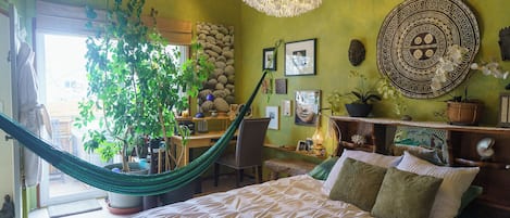A bedroom with a bed, a hammock, a desk, and various decorative items.