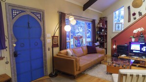 Een woonkamer met een blauwe deur, een bruine bank, een glazen salontafel en een televisie op een houten dressoir.