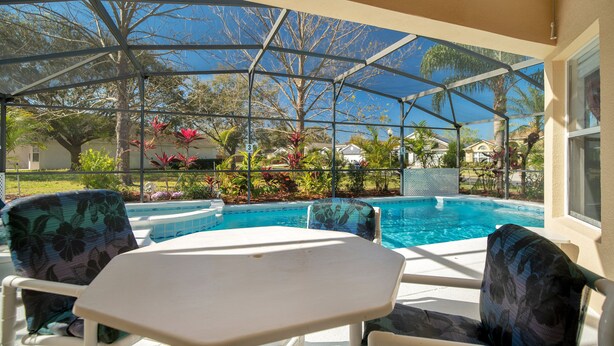 Un espacio exterior cubierto con piscina, sillas y una mesa.