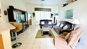 Una sala de estar con un sofá, una mesa de centro y un televisor. Hay una zona de comedor con una mesa y sillas.