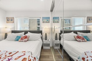 A hotel room with two beds, a mirror, and artwork on the walls.