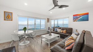 Un soggiorno moderno con vista sull'oceano, una zona pranzo con tavolo rotondo e un divano con cuscini decorativi.