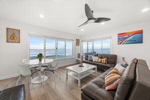 A modern living room with a view of the ocean, a dining area with a round table, and a sofa with decorative pillows. - Right on the Famous Mission Beach Boardwalk - Sleeps up to 10 on Top Floor - Best location in Mission Beach (San Diego)