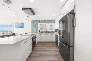 A modern kitchen with a large island, stainless steel appliances, and a view of the ocean through the window. - Right on the Famous Mission Beach Boardwalk - Sleeps up to 10 on Top Floor - Best location in Mission Beach (San Diego)