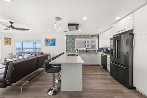 A modern kitchen with a central island, bar stools, a refrigerator, and a view of the ocean.