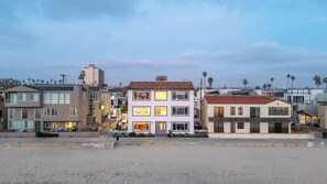 A beachfront residential area with modern houses, a sandy beach, and palm trees. - Right on the Famous Mission Beach Boardwalk - Sleeps up to 10 on Top Floor - Best location in Mission Beach (San Diego)