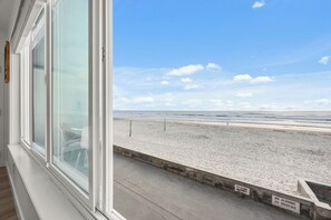 A view of a beach from inside a building, with a clear sky and a sign indicating no glass bottles, no alcohol, and no smoking.