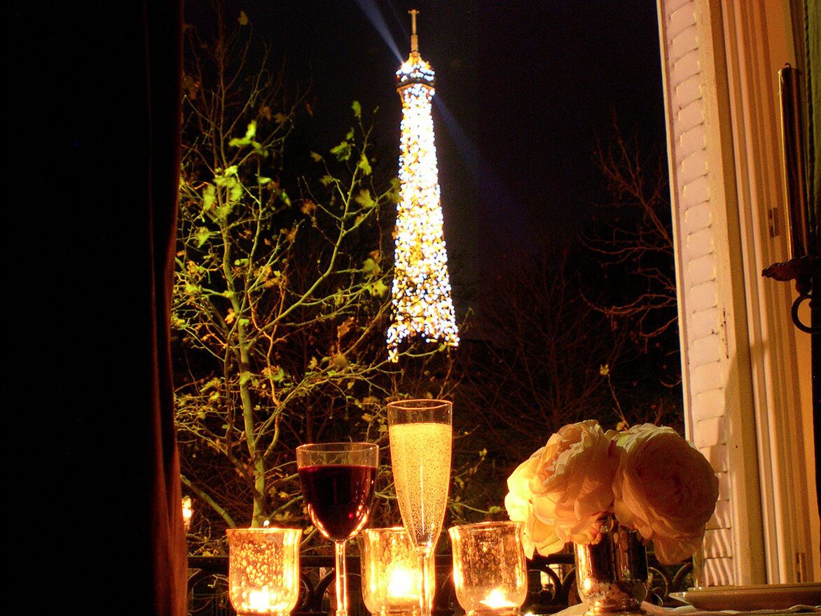 A table with glasses and a candle, a rose, and an illuminated tower in the background.