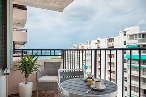 Een balkon met uitzicht op zee, een ronde tafel met kopje en schotel, en een rieten stoel.