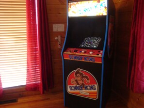 Un juego de arcade antiguo llamado 'Donkey Kong' en una habitación con paredes de madera y cortinas rojas.