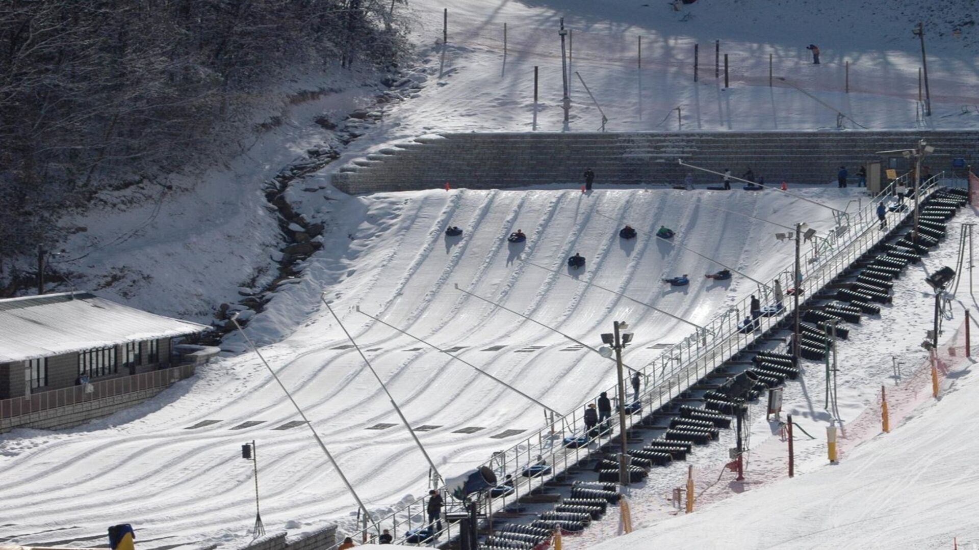 A ski lift with chairs and a cable system, surrounded by snow-covered slopes and a building with a sloped roof.