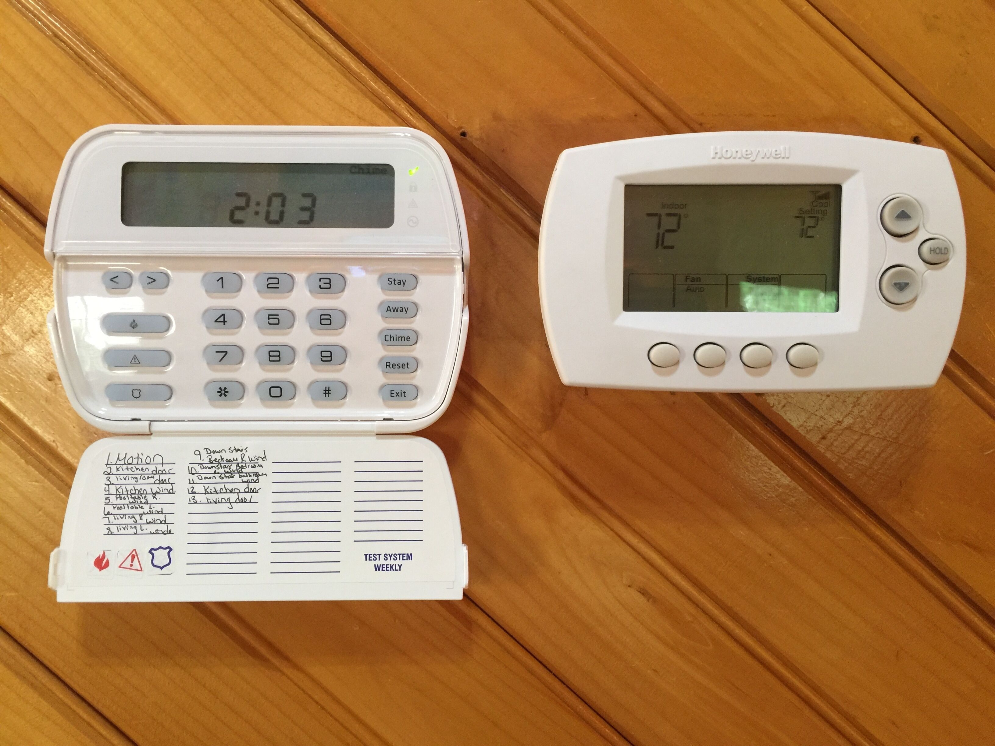 Two white electronic devices on a wooden surface. One is a digital clock displaying 2:03, and the other is a thermostat showing 72 degrees.