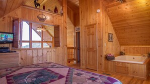 Een houten slaapkamer met een groot bed, een raam, een deur en een badkamer met een bad.