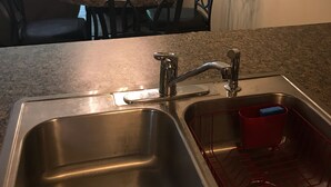 Una cocina con un lavamanos de acero inoxidable, una mesa de comedor con sillas y una araña.