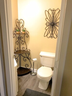 Ein kleines Badezimmer mit Toilette, einem dekorativen Metallregal mit Pflanzen und einem Wandbild.