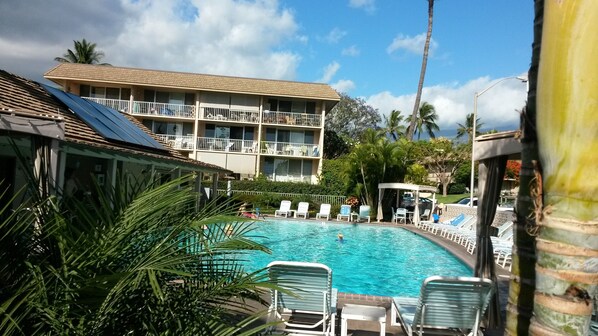 A hotel with a swimming pool surrounded by lounge chairs, palm trees, and a multi-story building with balconies.